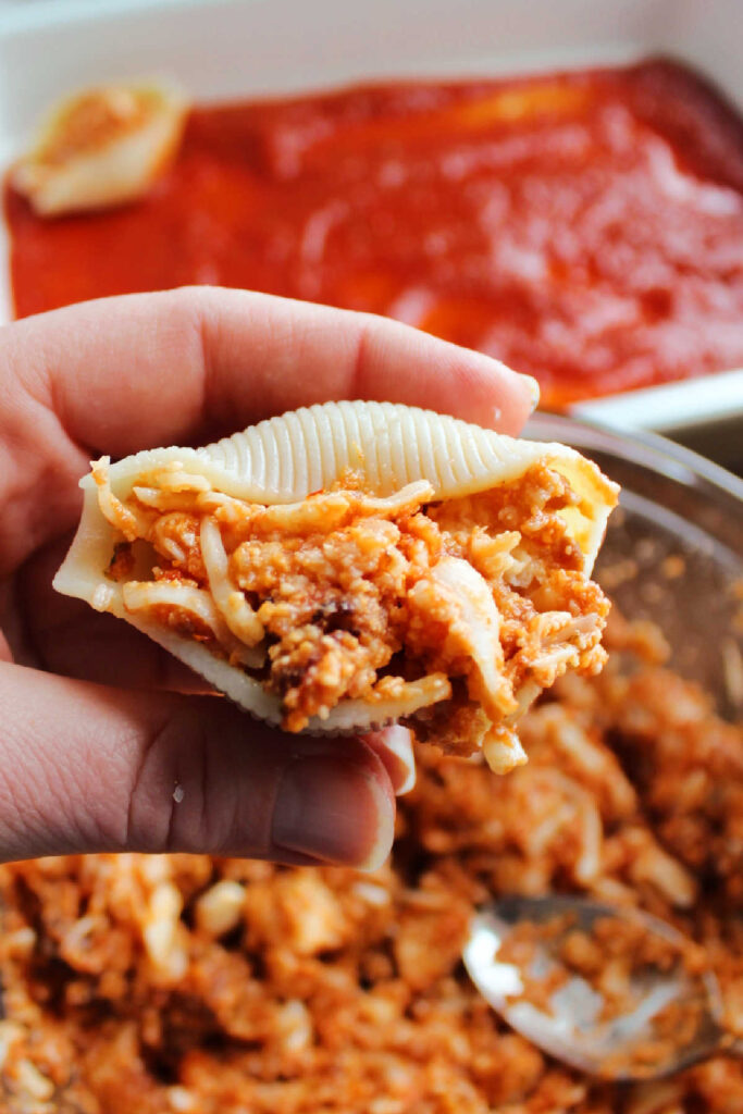 Hand holding shell filled with chopped chicken cheese and tomato sauce mixture.