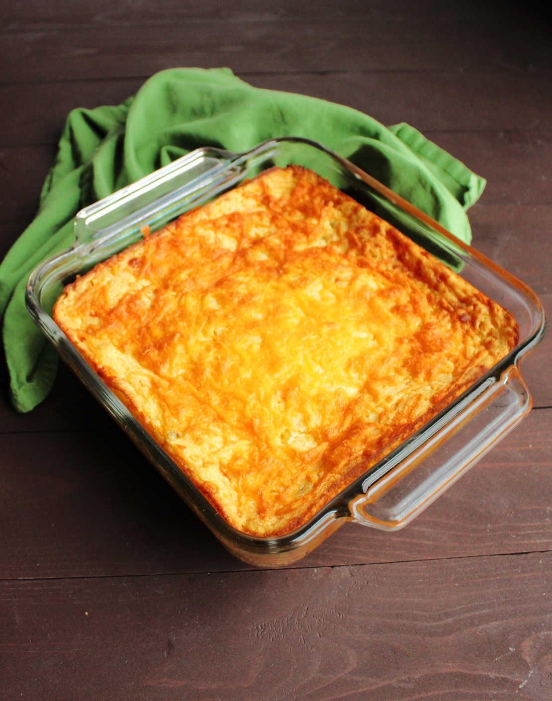 Pan of freshly baked green chile corn casserole with melted cheddar cheese on top.