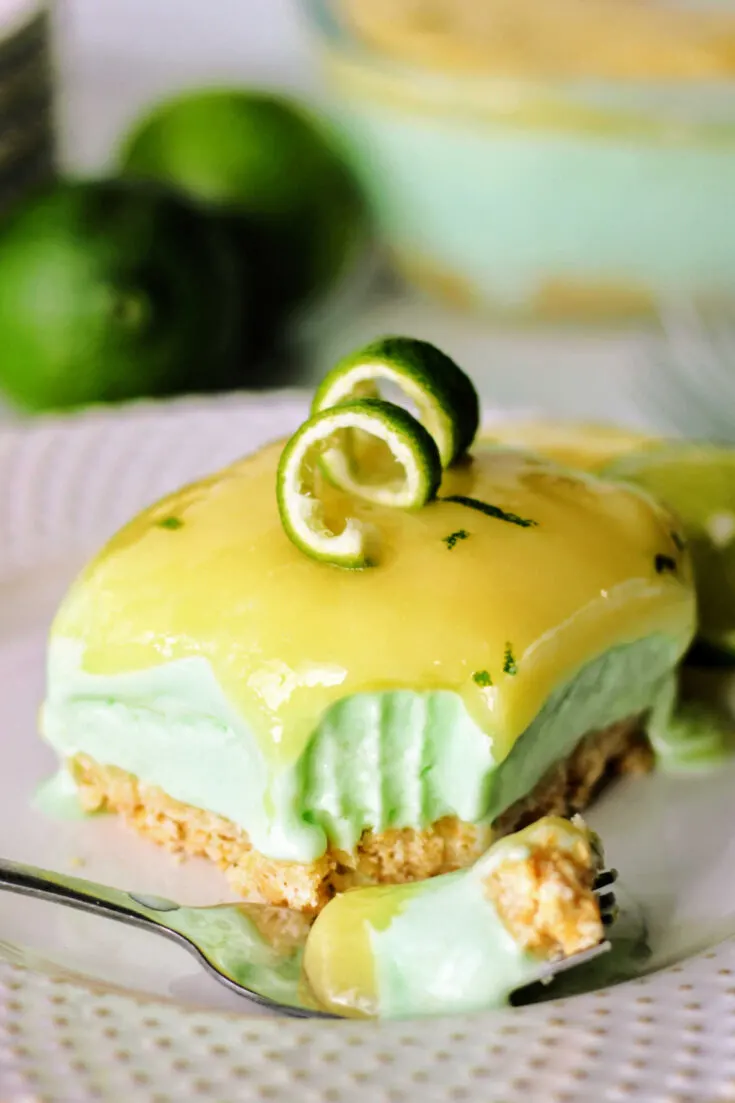 bite of layered lime sherbet bar on fork showing cracker crust, creamy sherbet center and bright lime curd topping.