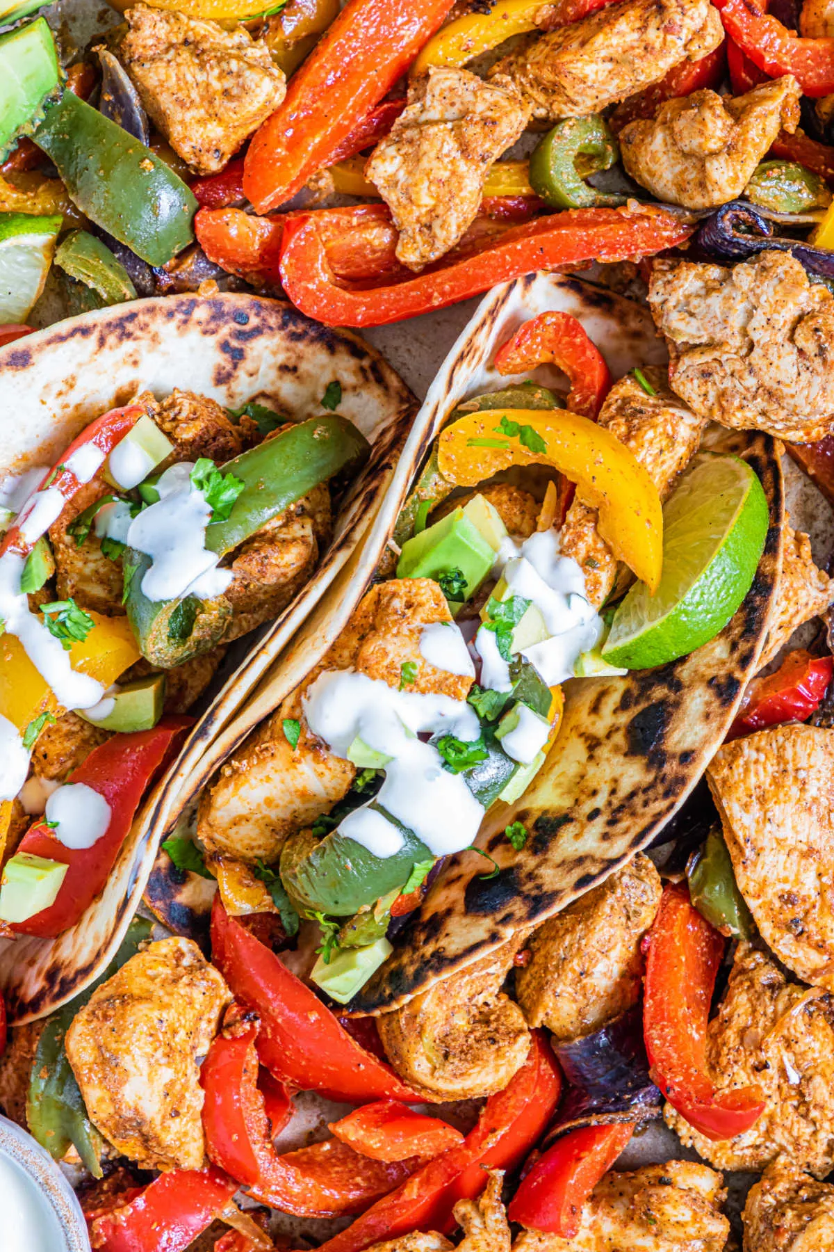 sheet pan chicken fajitas in tortillas with sour cream, lime wedges and cilantro.