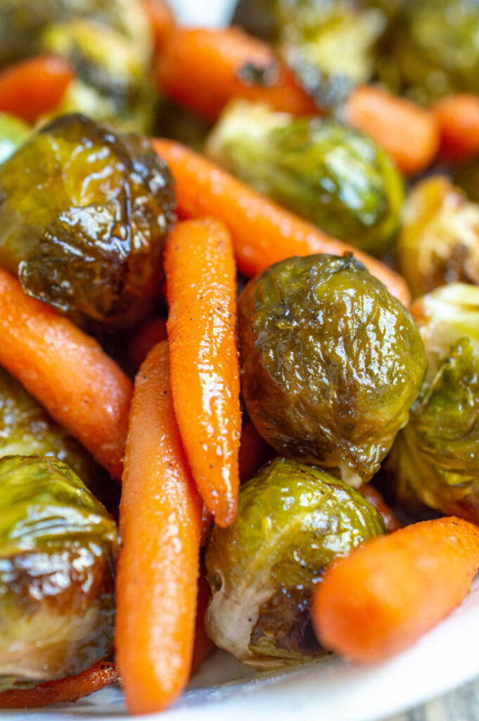 Close up of shiny honey roasted baby carrots and brussels sprouts.