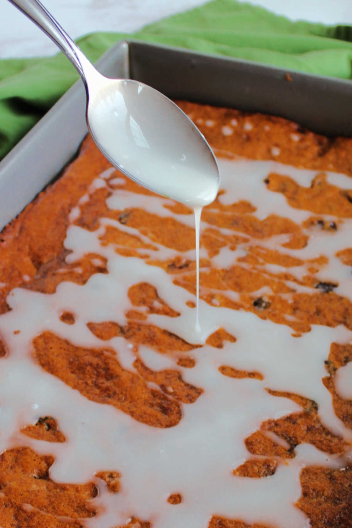 spoon drizzling powdered sugar glaze over raisin depression cake. 