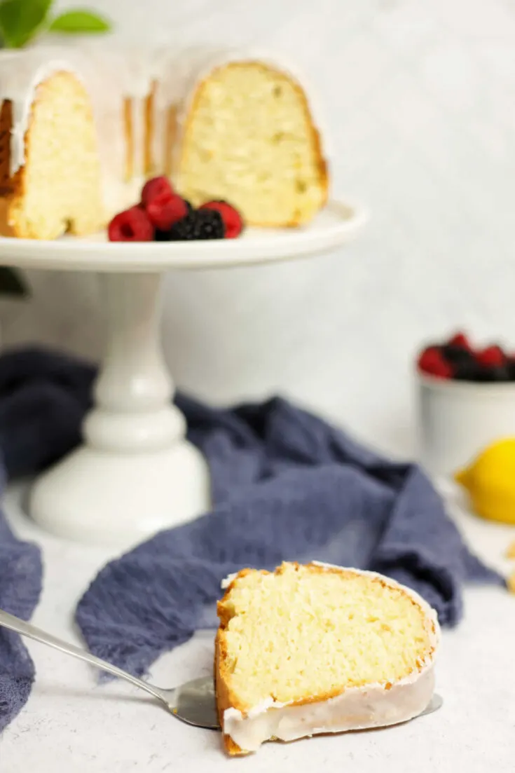 Slice of lemon bundt cake with remaining cake in background.