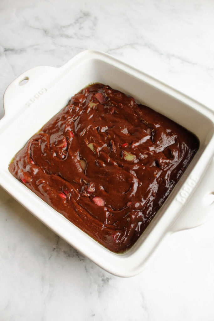 Rhubarb brownie batter in square baking dish, ready to go in the oven.