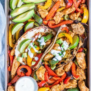 Sheet pan filled with chicken fajita fixings with avocado wedges, limes and sour cream.