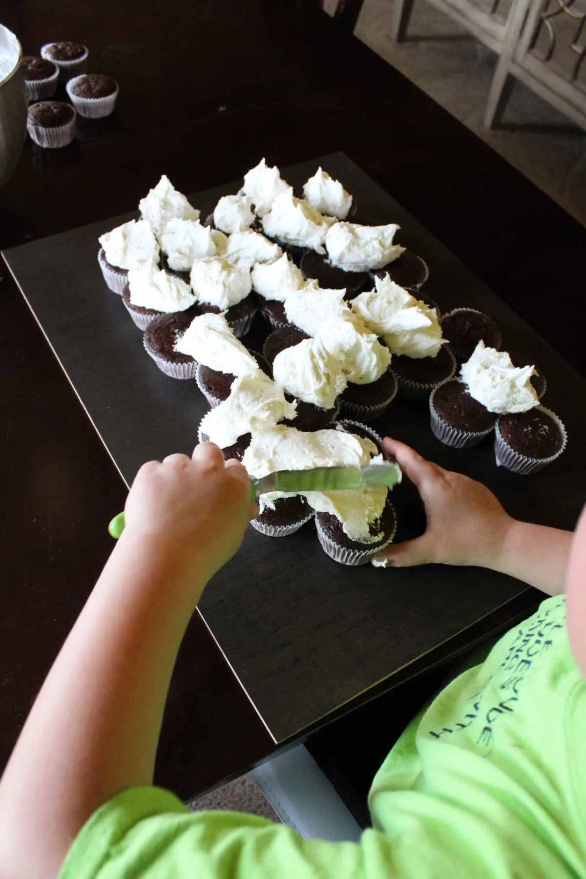 Starting to spread out scoops of frosting over arranged cupcakes.
