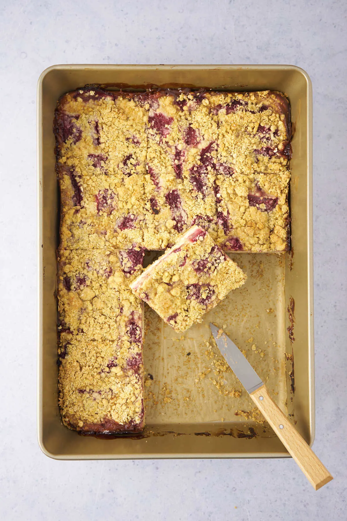 piece of strawberry yogurt bars with crumb topping with piece on spatula.
