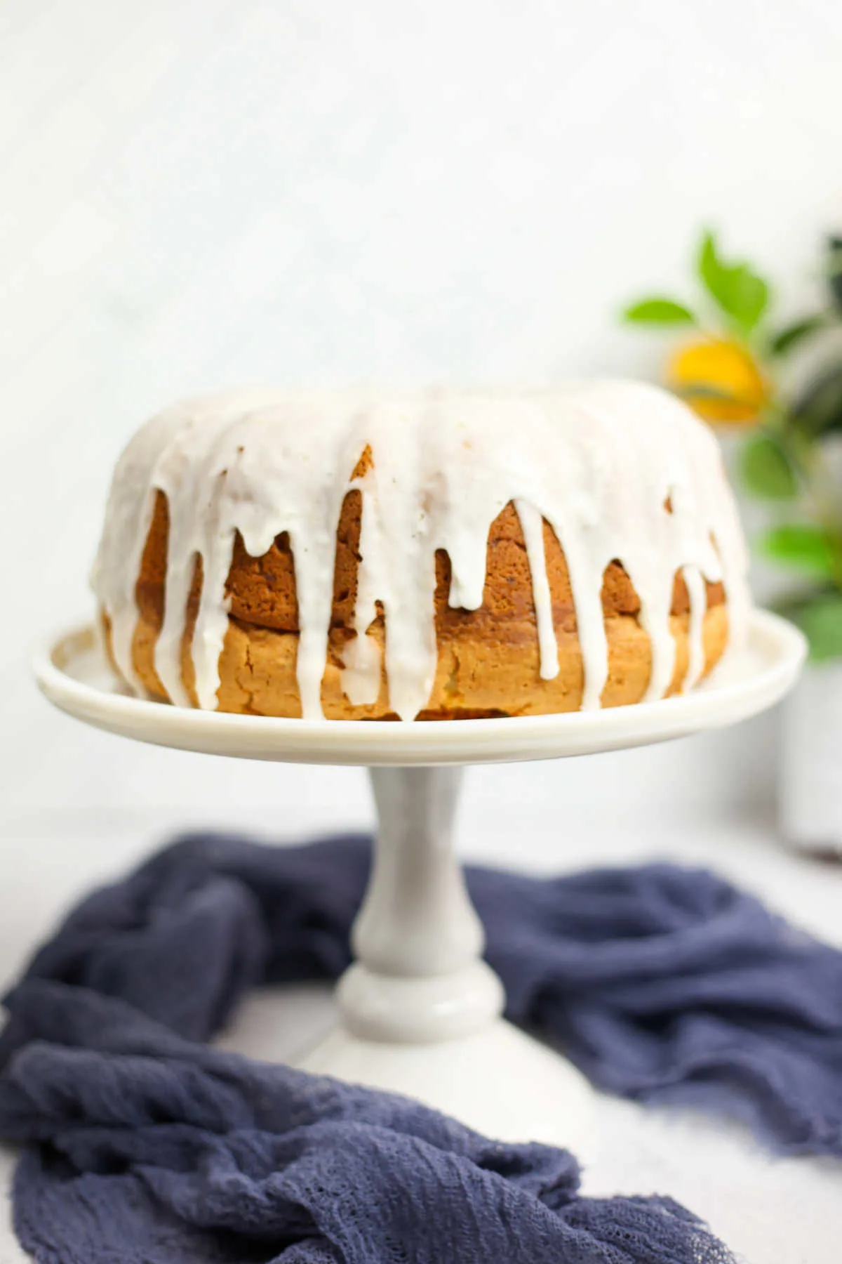 Whole lemon bundt cake with white lemon ginger glaze on top of cake stand.