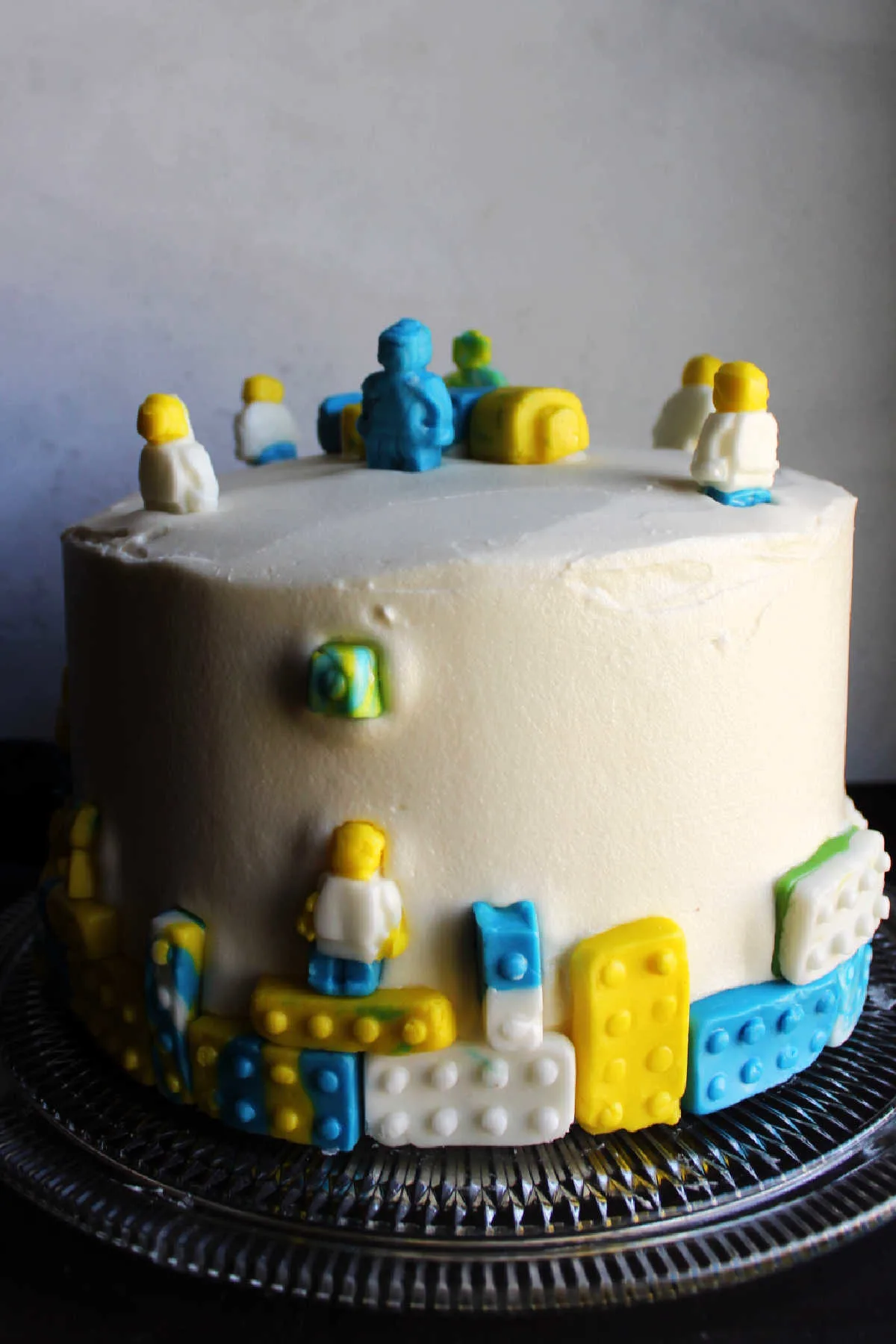 Layer cake frosted with white marshmallow buttercream decorated with fondant legos and lego guys.