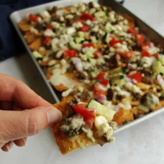 Sheet pan filled with gyro inspired nachos topped with feta, cucumbers, tomatoes, tzatziki and more.