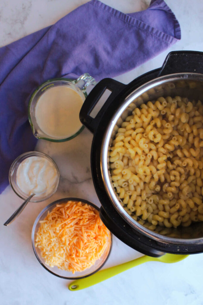 Instant pot filled with water and pasta next to bowls of cheese, sour cream and milk.