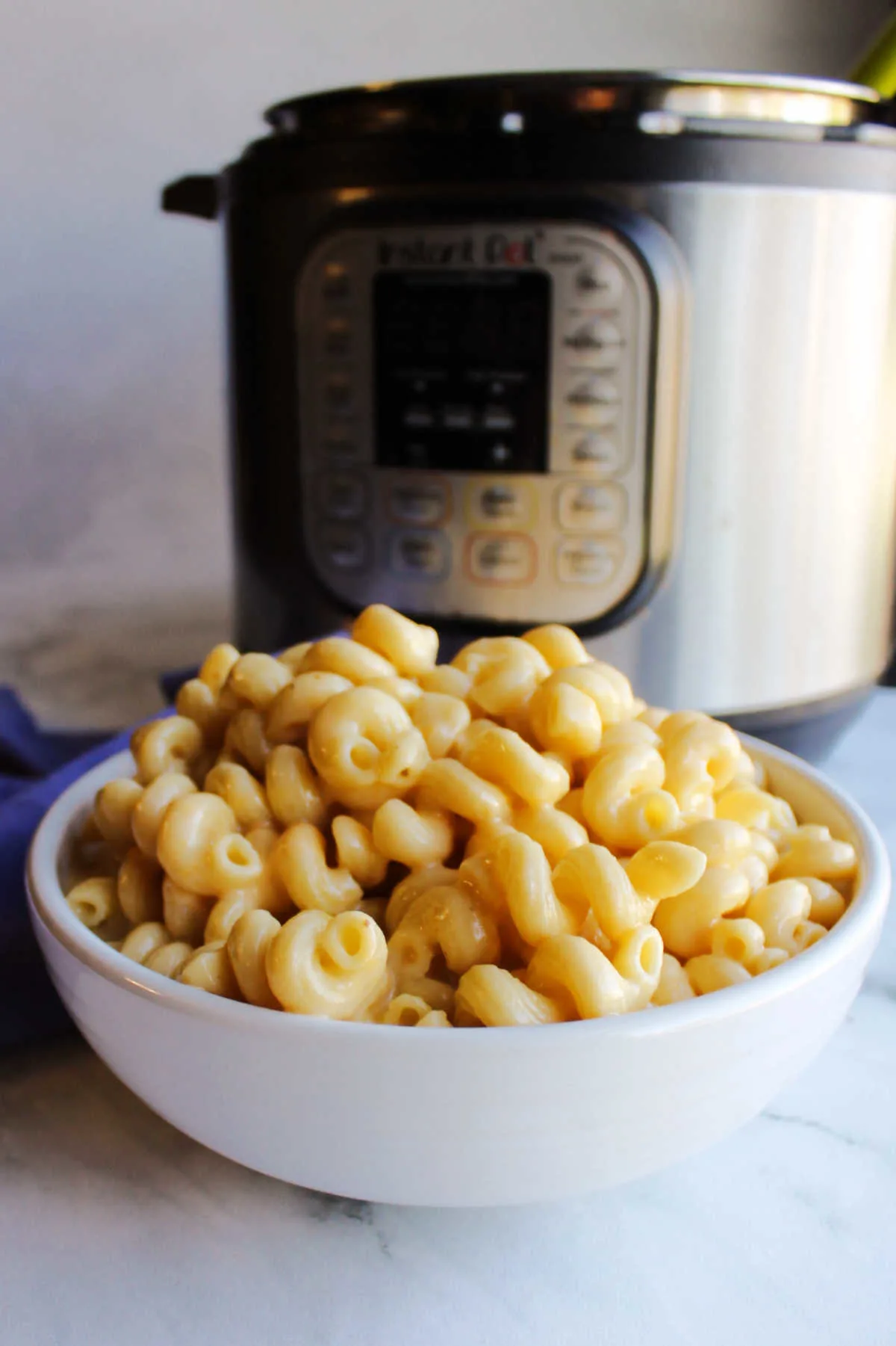 Close up of serving bowl filled with creamy macaroni and cheese by pressure cooker.