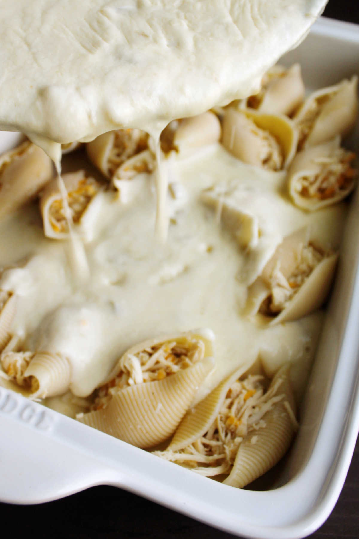 Pouring sour cream cheese sauce over stuffed shells.