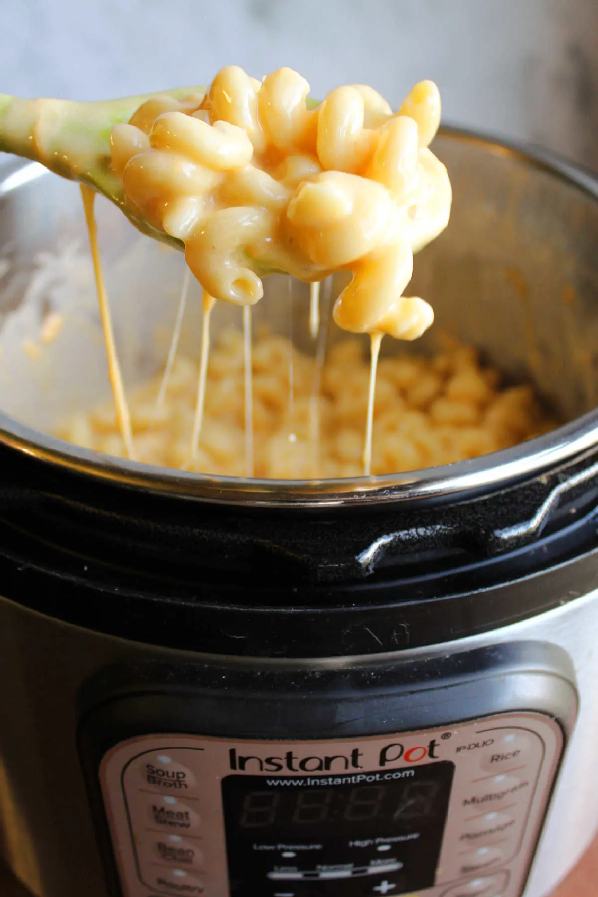 Spoon lifting curly mac and cheese instant pot with several cheese pulls coming from the pot showing rich, cheesy sauce.
