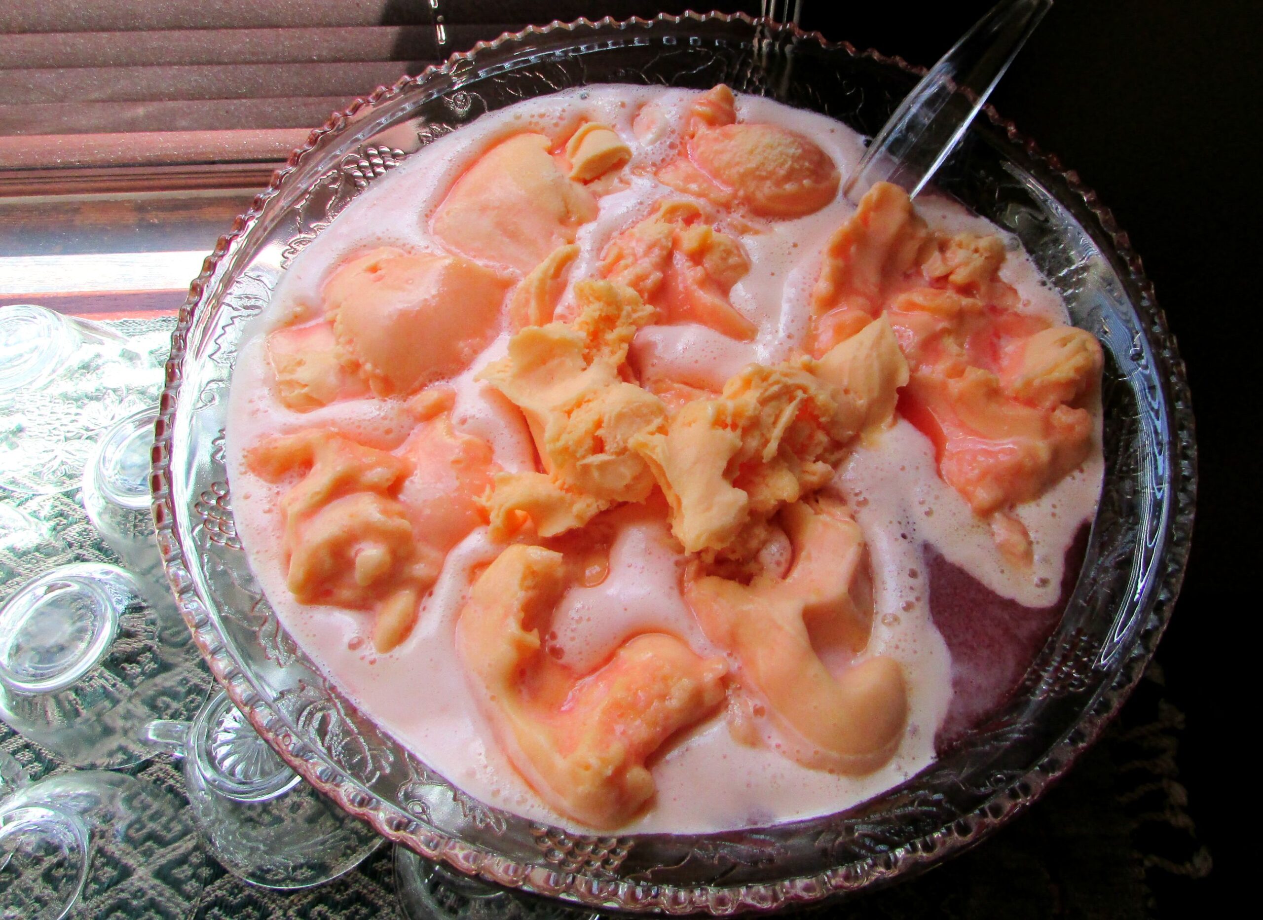 large glass punch bowl filled with pink punch topped with scoops of orange sherbet.