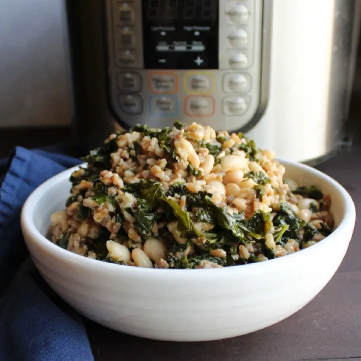 bowl of farro with kale, Italian sausage, white beans and Parmesan cheese in front of instant pot.
