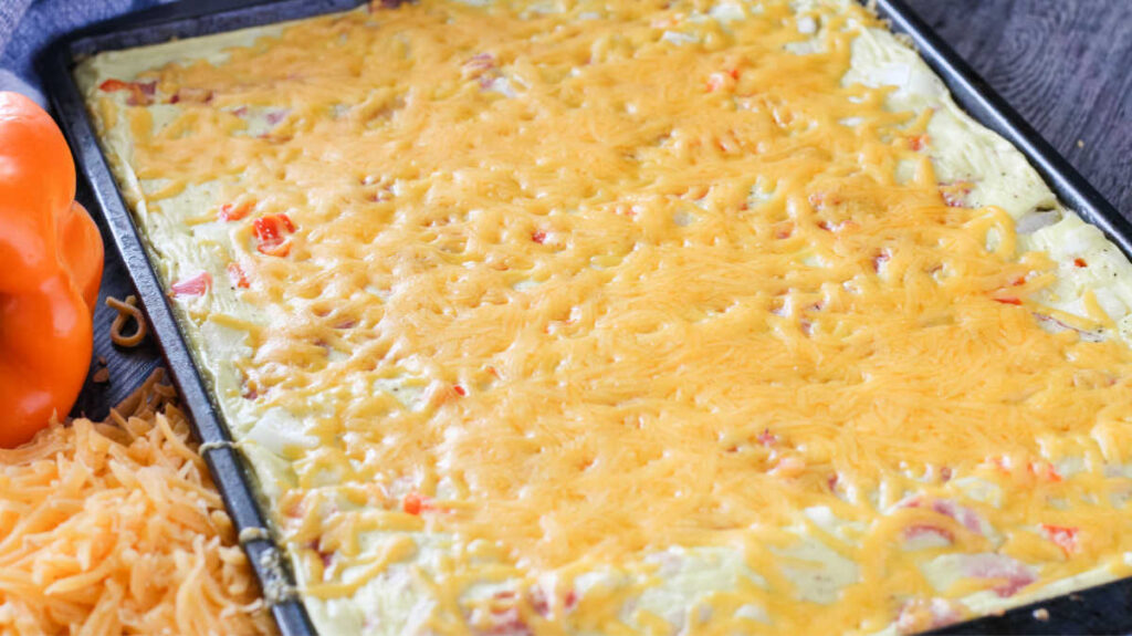 Melted cheese over sheet pan omelet mixture with eggs, ham, pepper and onions.