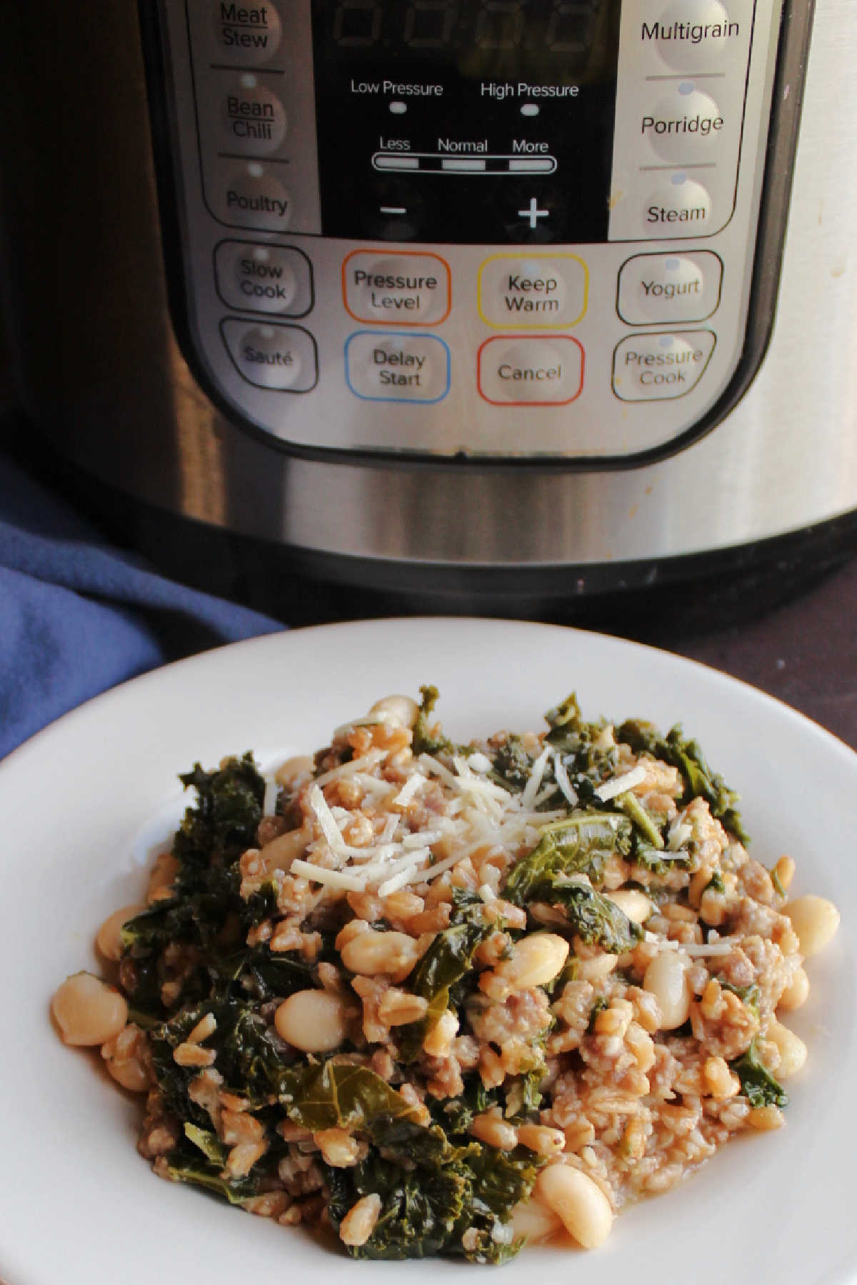 Plate of farro with Italian sausage, kale, white beans and Parmesan cheese in front of pressure cooker. 
