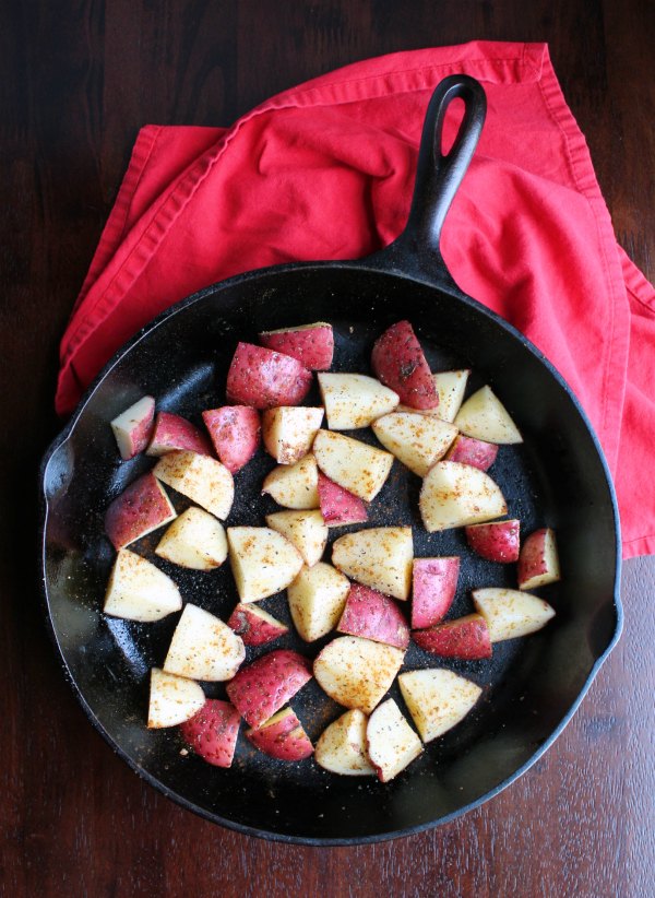 Chunks of seasoned red potatoes in cast iron skillet ready to go in the oven.