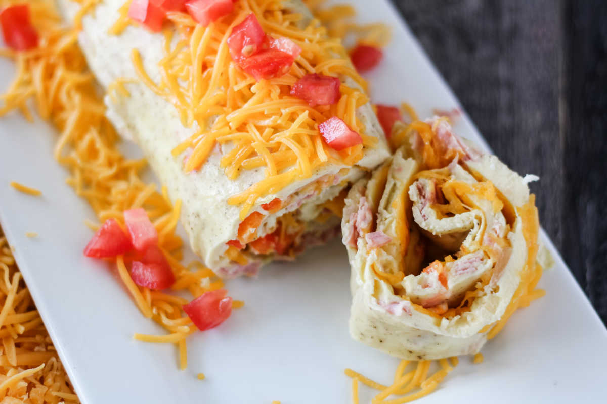 Cutting slice off of Denver omelet roll with layers of egg, cheese, peppers and more.