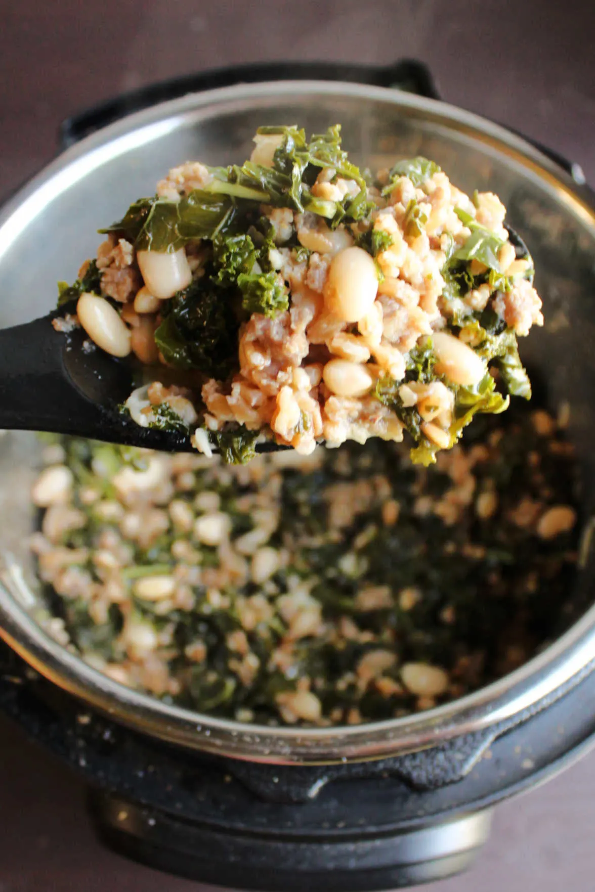 Spoonful of farro with kale and sausage being lifted out of instant pot.