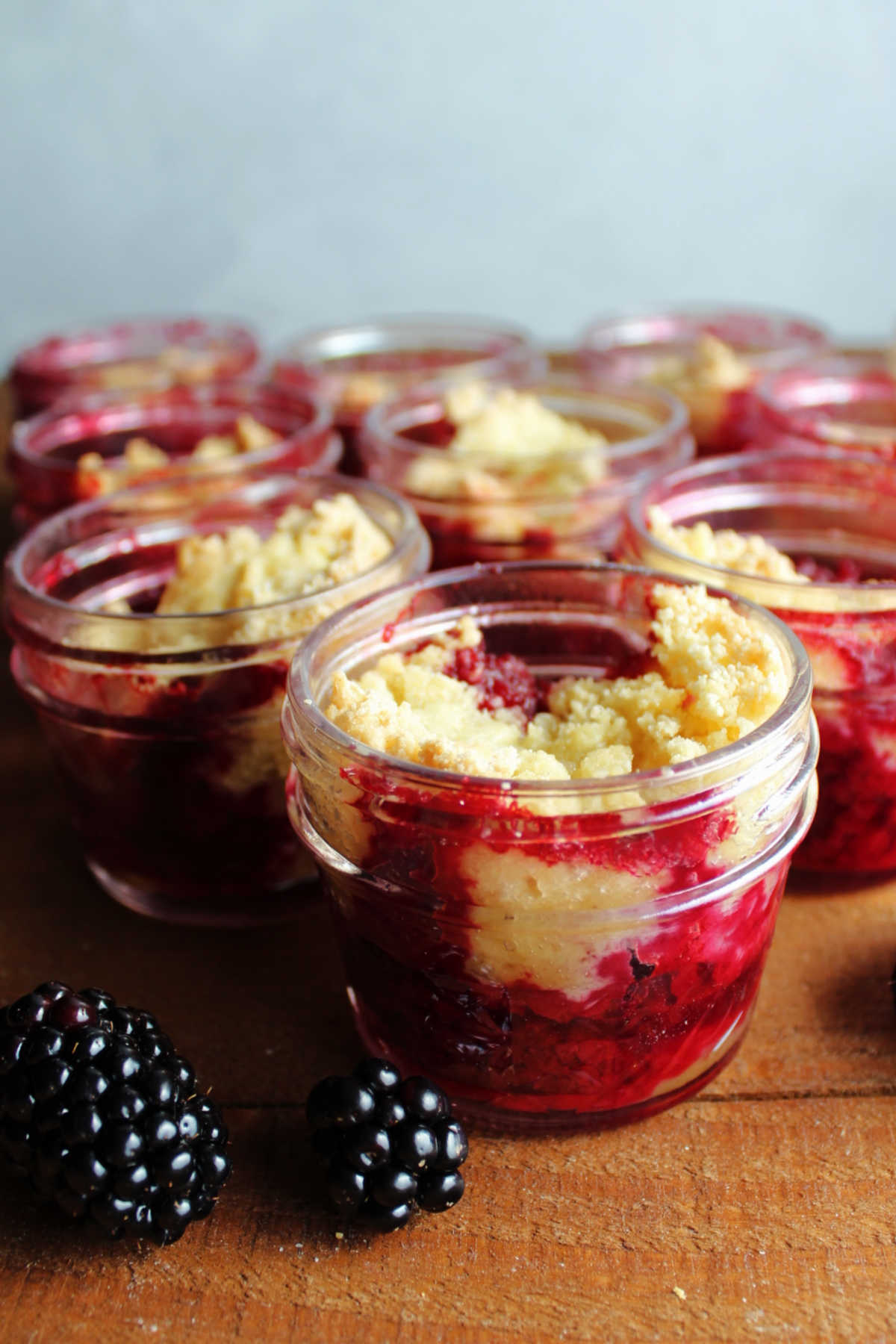 Looking at bright purple blackberry filling under golden cobbler topping in small glass jars.