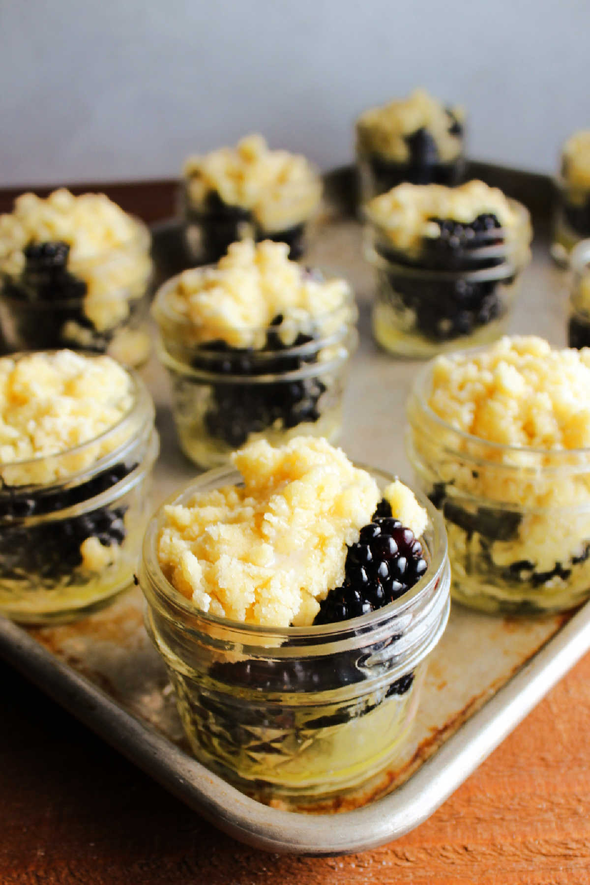Fresh blackberries topped with buttery cobbler mixture in small glass jars ready to bake.