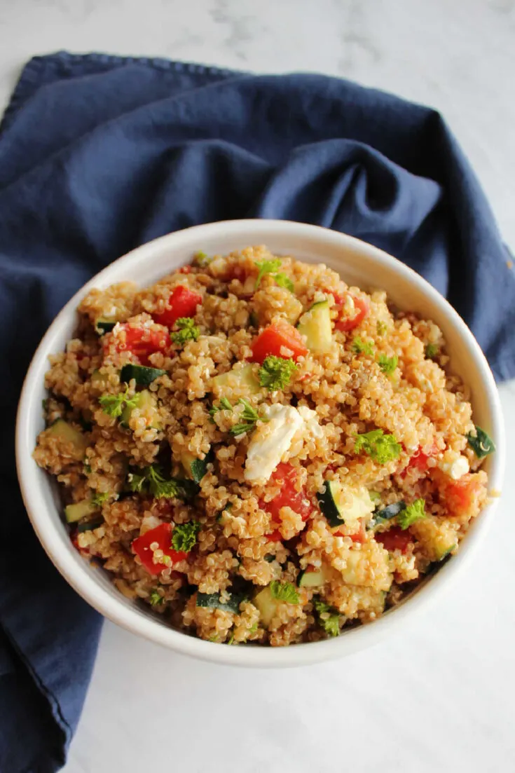 Serving bowl of quinoa salad with tomatoes, cucumbers, feta cheese and more.