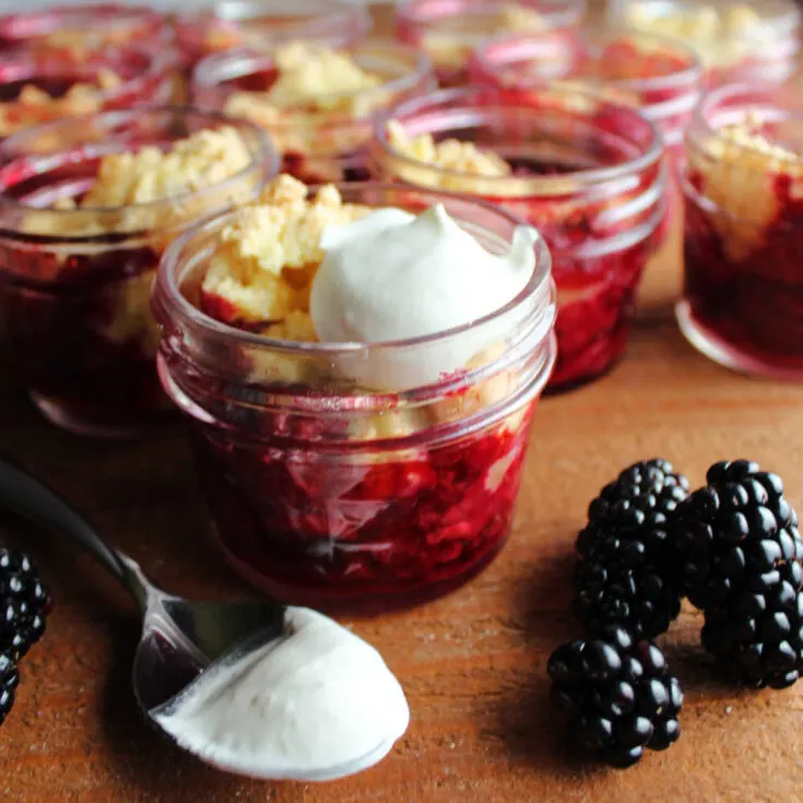 Close look at jars of blackberry cobbler with whipped cream.