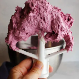 Mixer paddle filled with freshly whipped blueberry buttercream ready to use.
