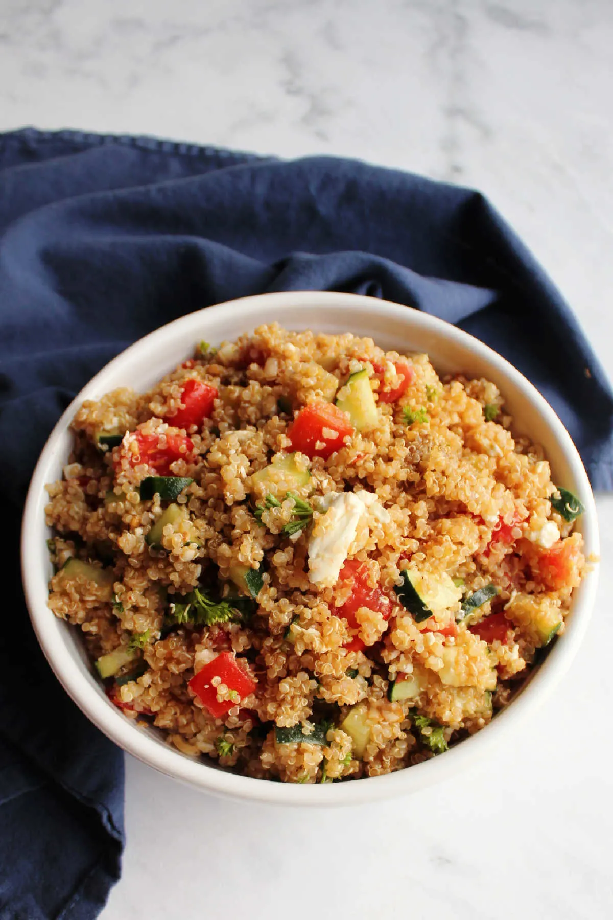 Large white serving bowl filled with quinoa salad with tomatoes, cucumbers and feta cheese.