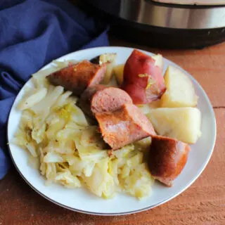 Plate filled with cooked sausage, potatoes and cabbage.