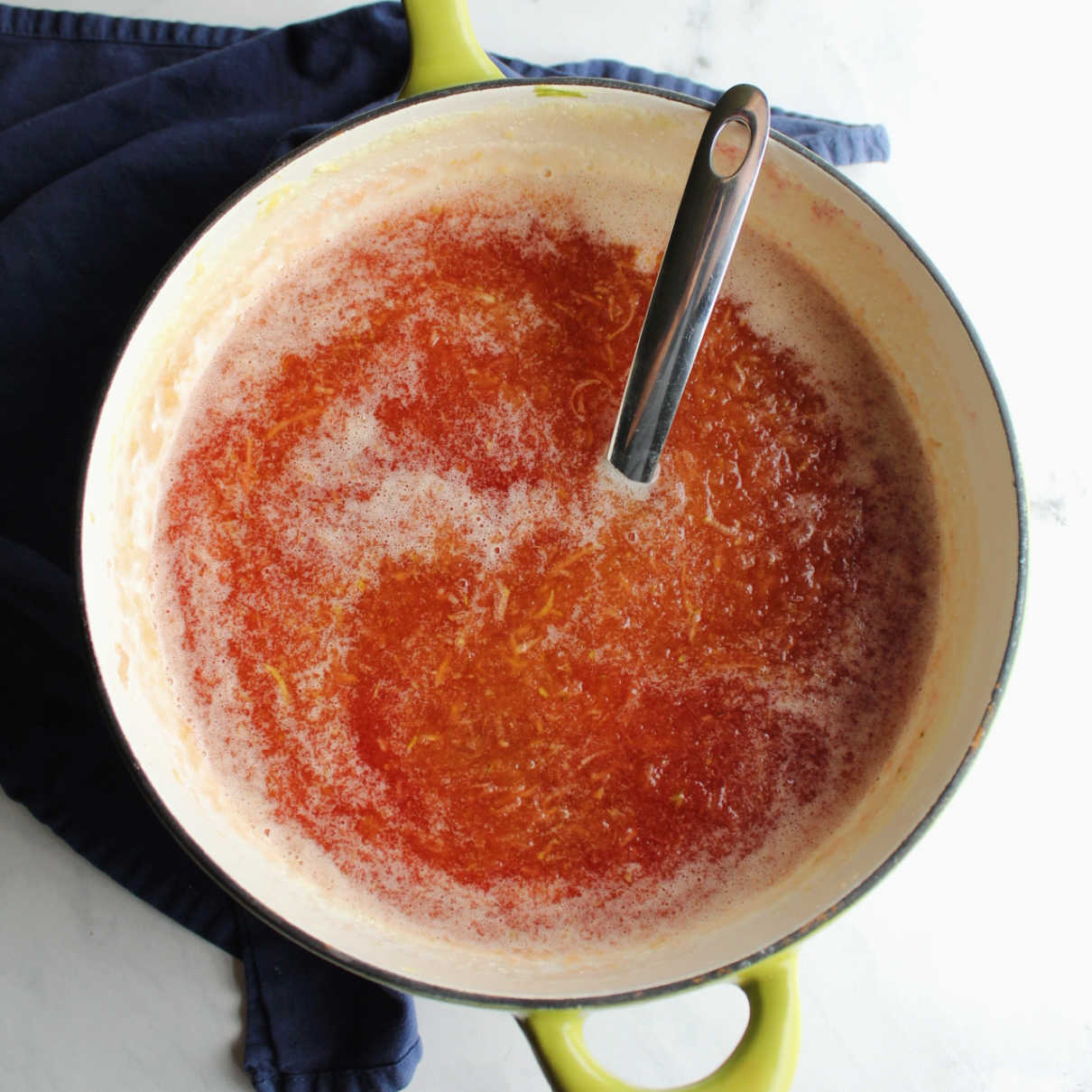 Saucepan filled with reddish peach colored jam inside and ladle ready to scoop it into jars.