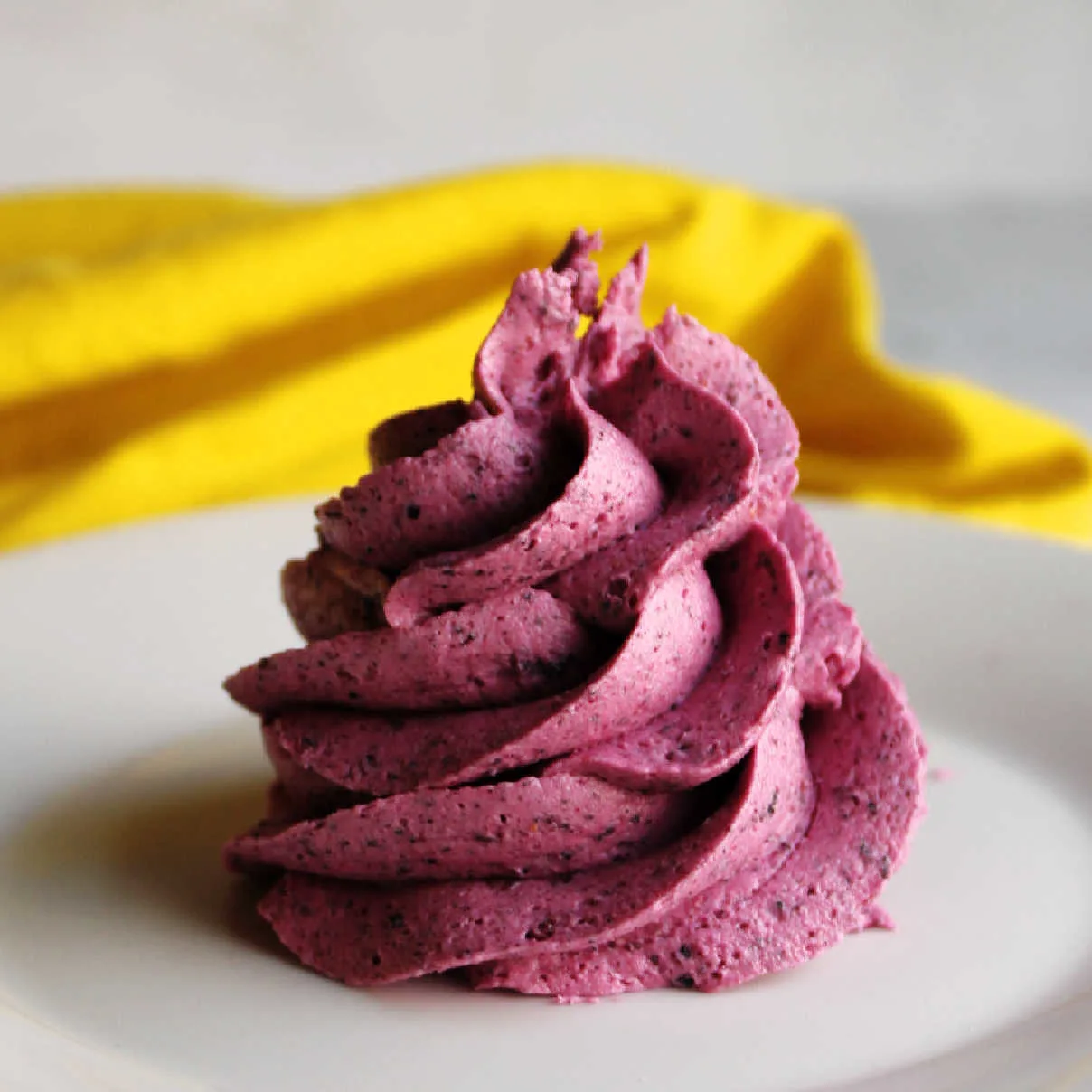 Close swirl of blueberry buttercream showing flecks of berry and deep purple color.