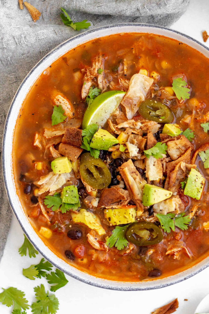 Close bowl of chicken tortilla soup topped with avocado, cilantro and lime.