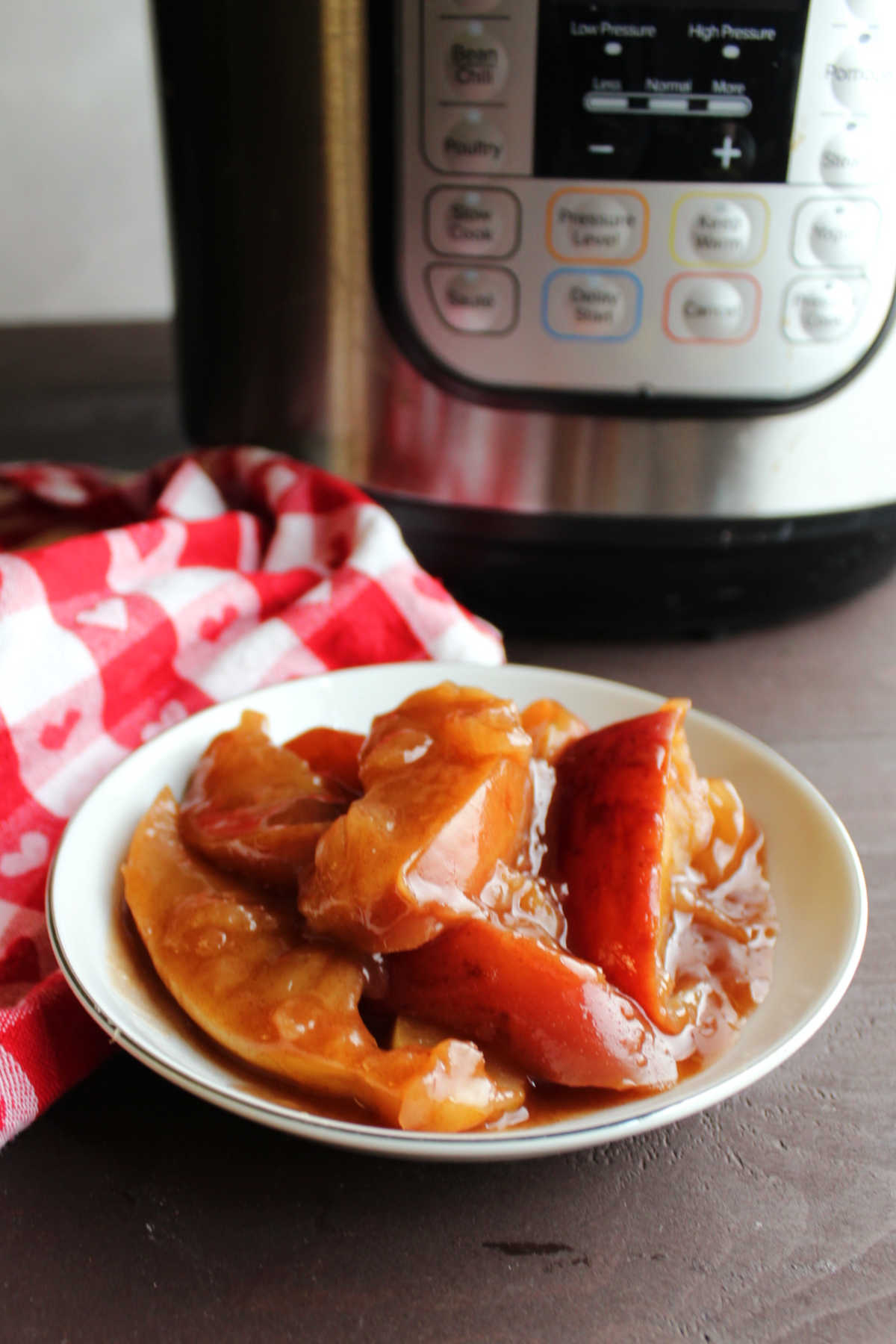 Bowl of cooked apples in thick cinnamon brown sugar sauce in bowl in front of instant pot.
