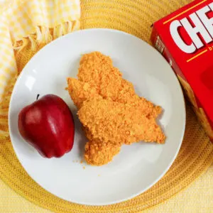 plate of cheez-it coated chicken fingers and apple ready to eat.