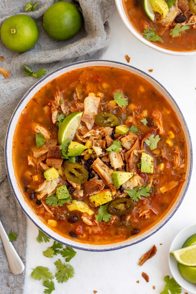 Big bowl filled with tomato based chicken tortilla soup with corn, black beans and more. 