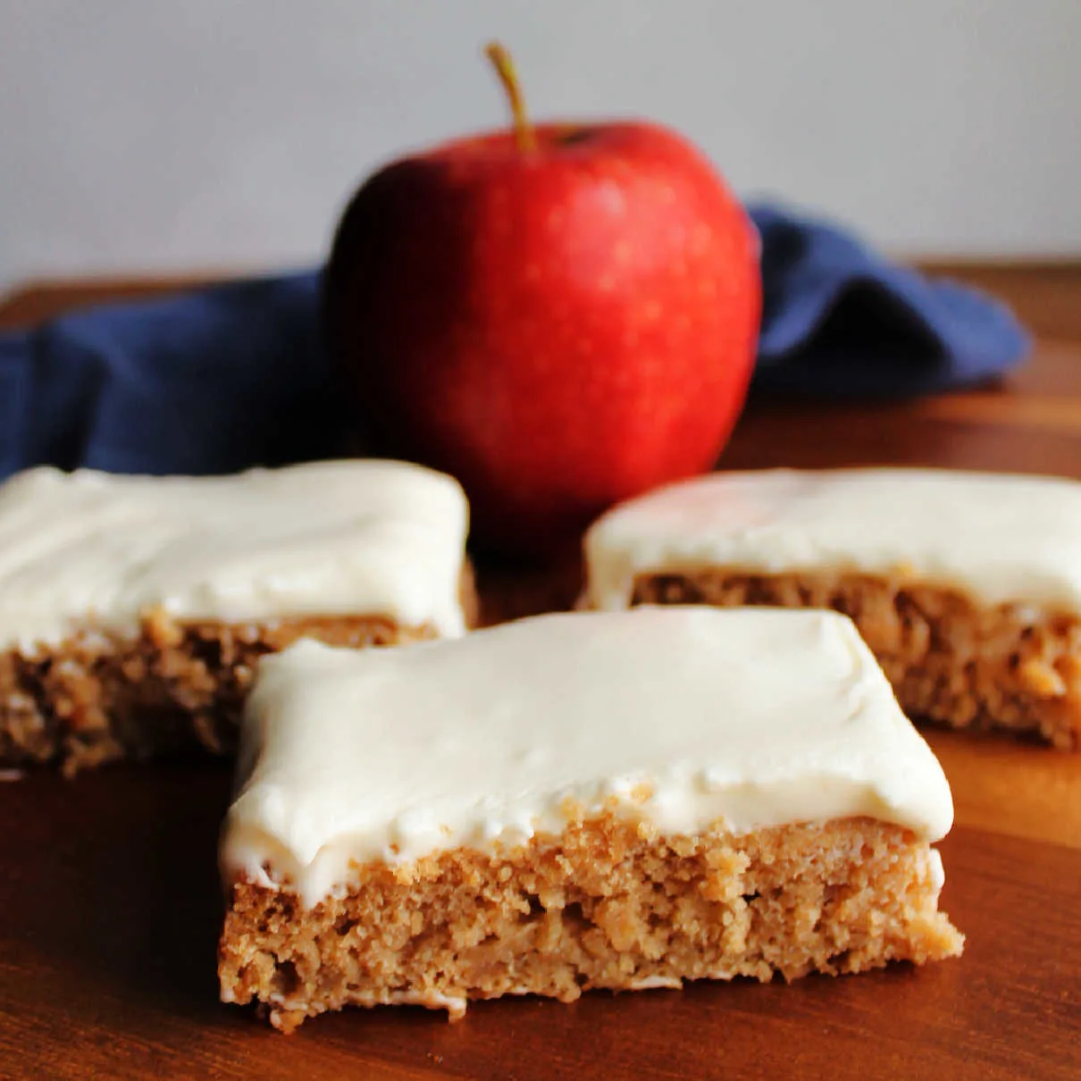 Pieces of applesauce cake topped with soft white sour cream frosting with an apple in the background.