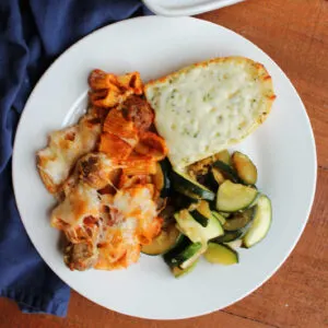 Dinner plate with no boil rigatoni and meatballs, sauteed zucchini and a hunk of cheesy garlic bread.
