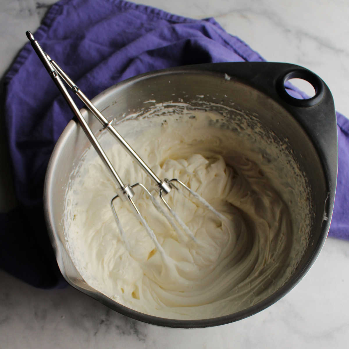 Mixing bowl filled with fluffy cream cheese whipped cream and beaters from mixer.