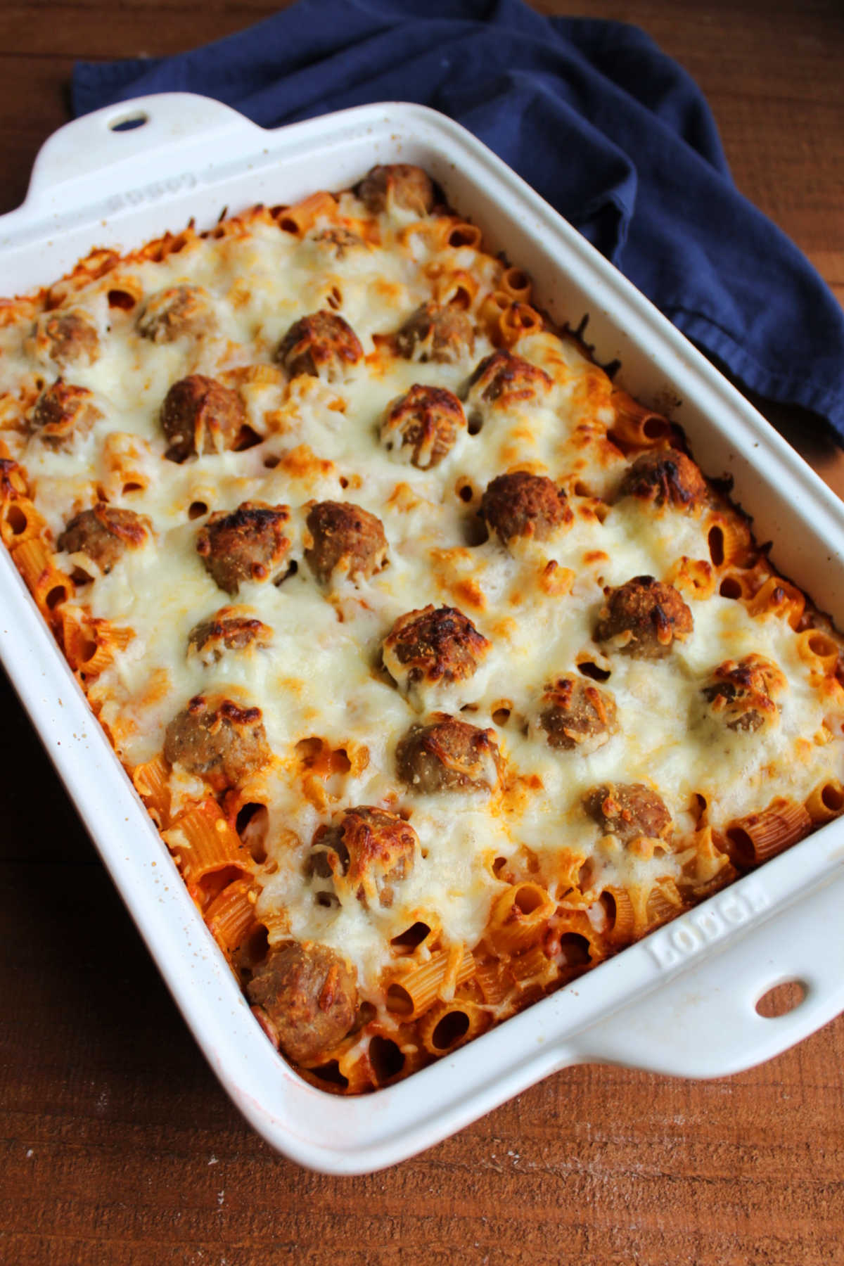 Baked pasta casserole with meatballs and golden brown melted cheese on top.