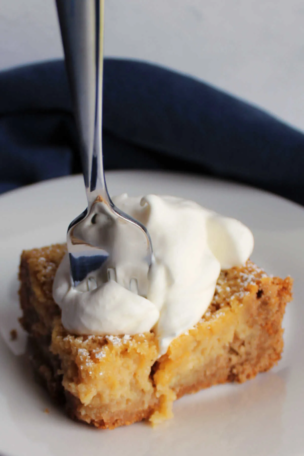 Fork going into piece of apple spice gooey butter cake topped with whipped cream.