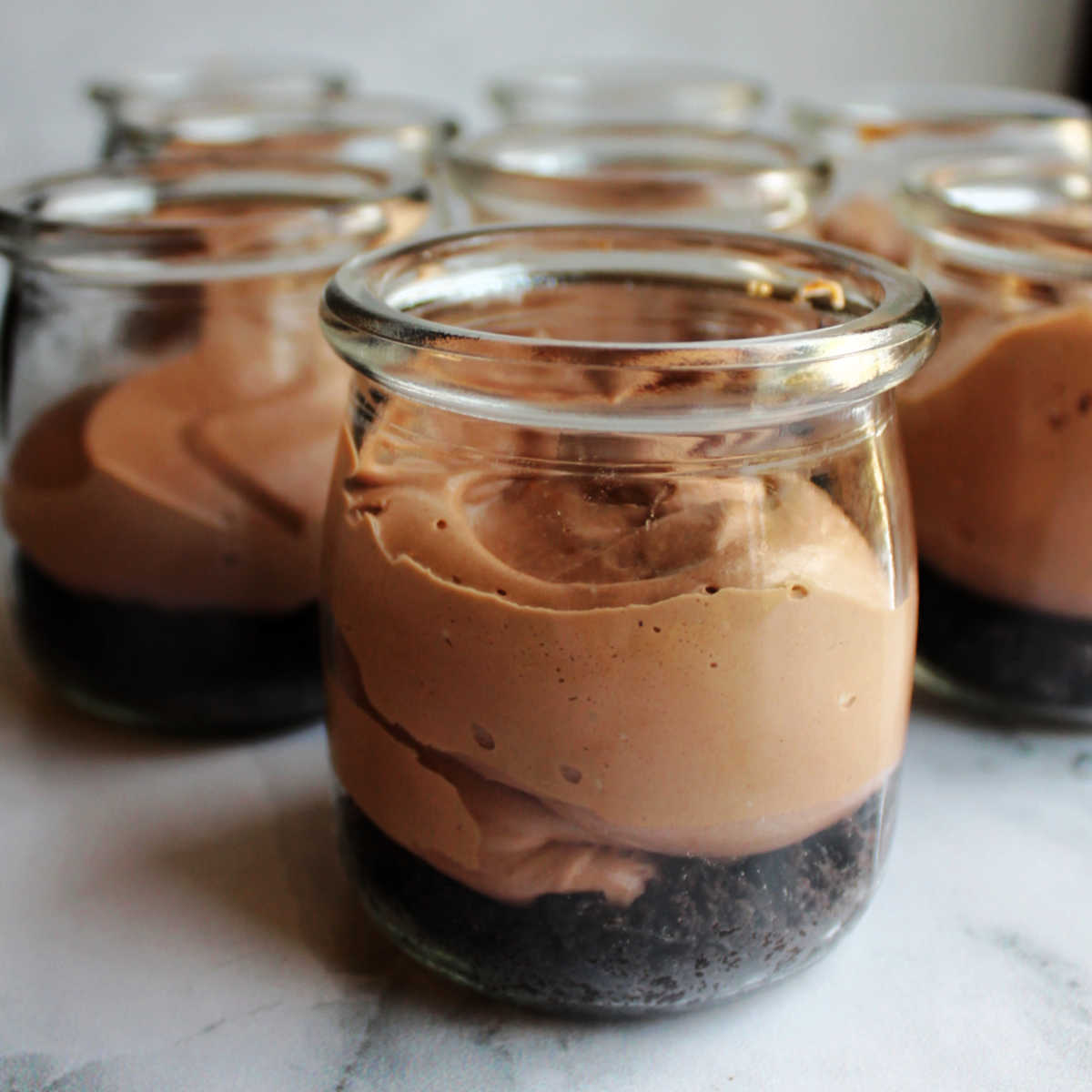 Jars with chocolate cookie crumb crust and chocolate cheesecake mixture piped on top.