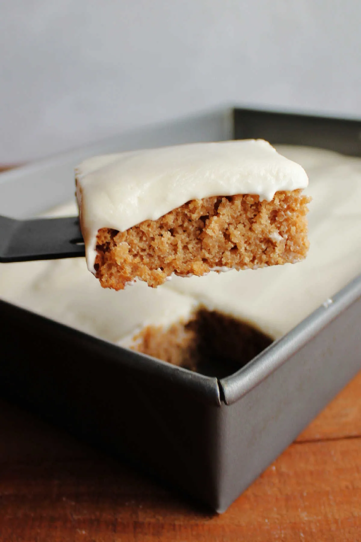 Lifting piece of apple bars topped with sour cream frosting out of pan.