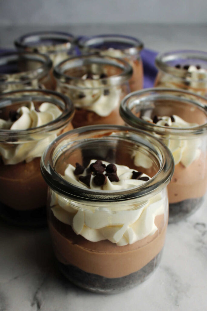 Collection of yogurt jars filled with chocolate cheesecake and whipped cream.