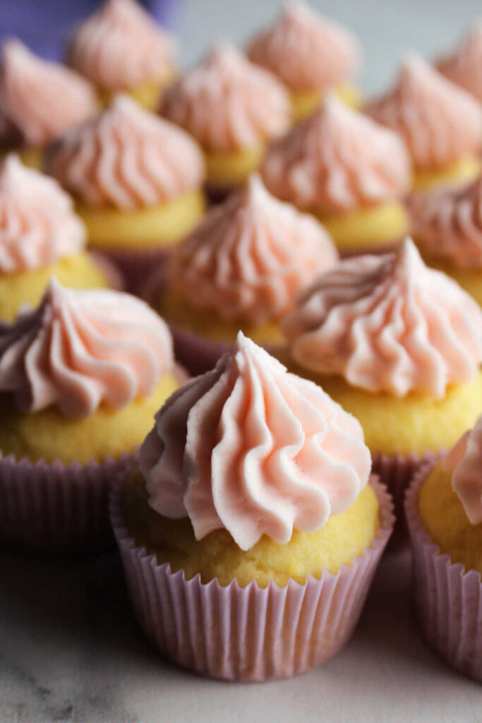 Mini cupcakes with dollops of pink lemon frosting on top.