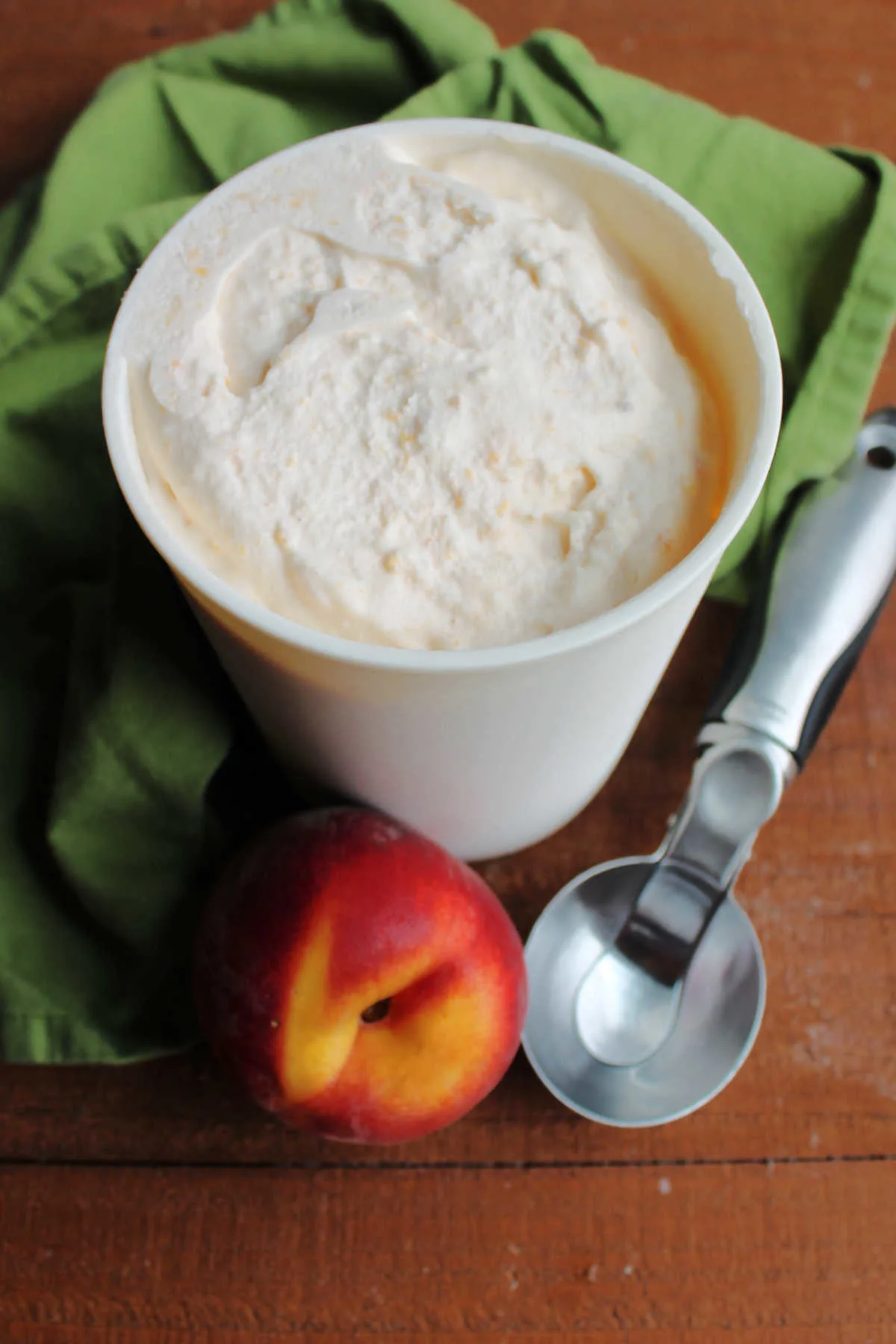 Container of fresh peach ice cream with a peach and scoop.