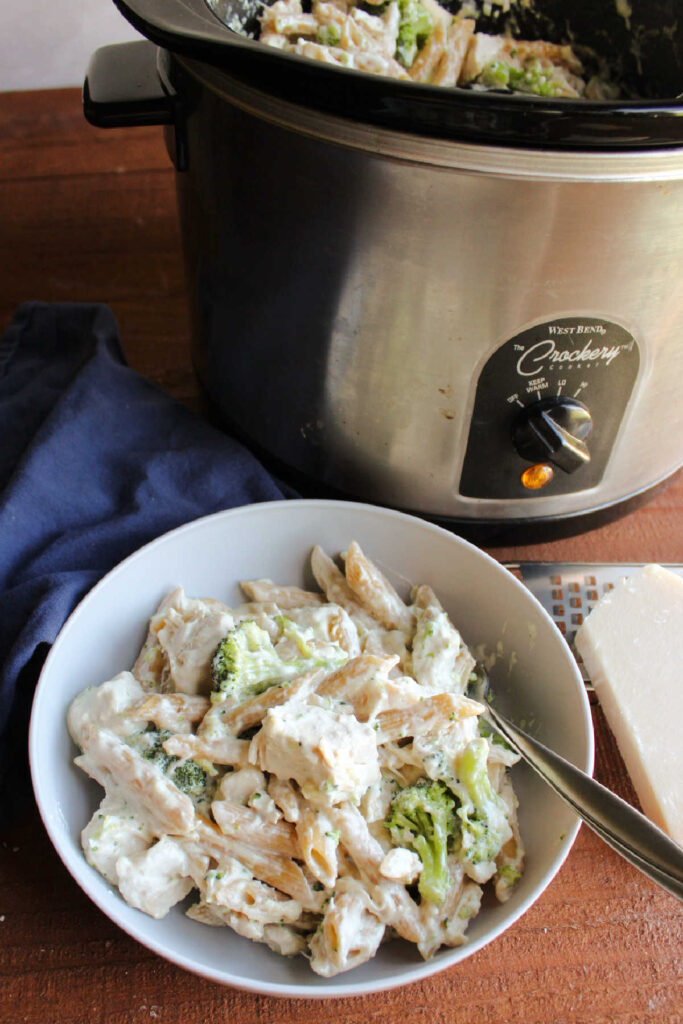 Looking down on slow cooker filled with chicken alfredo with pasta and broccoli, ready to serve and eat.