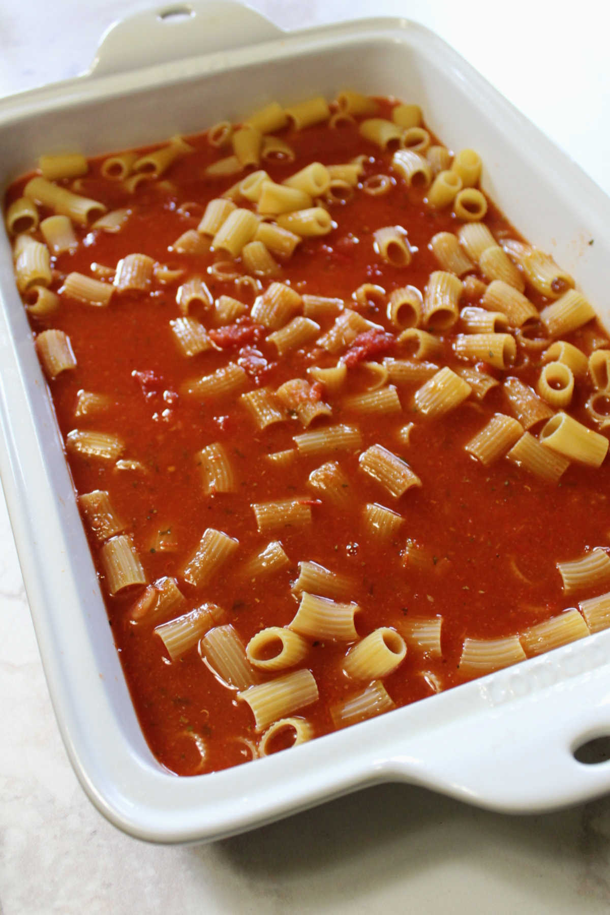 uncooked pasta and tomato sauce in baking dish ready for oven.